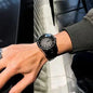 Person wearing a black wristwatch with a textured face, standing next to a car.