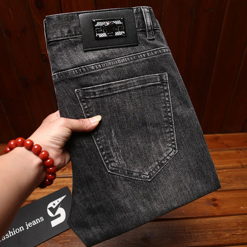 Black jeans held by a hand on a wooden surface with a brand tag visible.